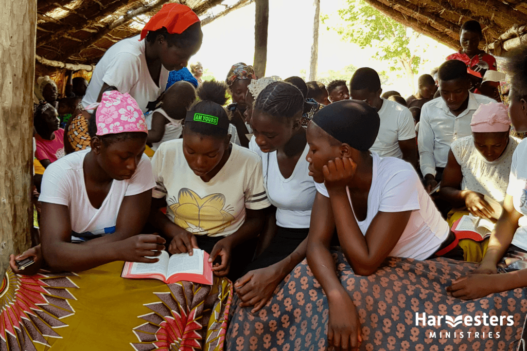 Ladies look at Bible together. Harvesters Ministries